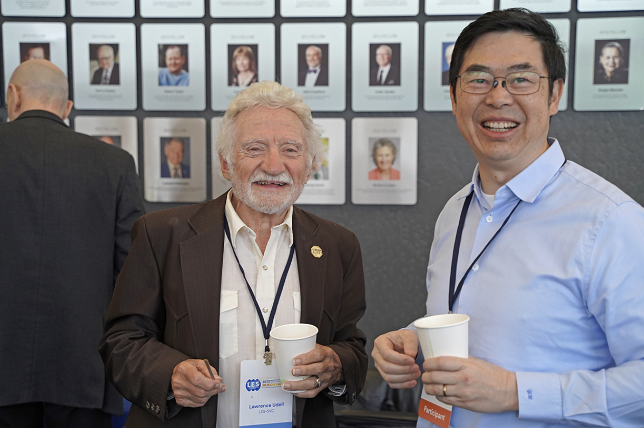 Larry Udell and another attendee, two members of LES, stand by a wall of portraits and drink from paper cups. They are at the Silicon Valley Deal Machine, an event hosted by the Silicon Valley Chapter, which brought together over 110 innovation leaders, IP professionals, and business dealmakers at the Computer History Museum in Mountain View, California.